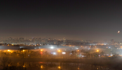 Fototapeta na wymiar Night cityscape of the big city. Awesome bright, multi colored light in thick fog at empty streets. Apartment buildings in bedroom community, commuter town area. Darnytsia, Kyiv. Ukraine. 2021