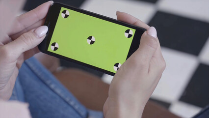 Chroma key screen for placement of your own content. Stock footage. Close-up of young woman sitting on the chair and looking at the phone with chroma key green screen.