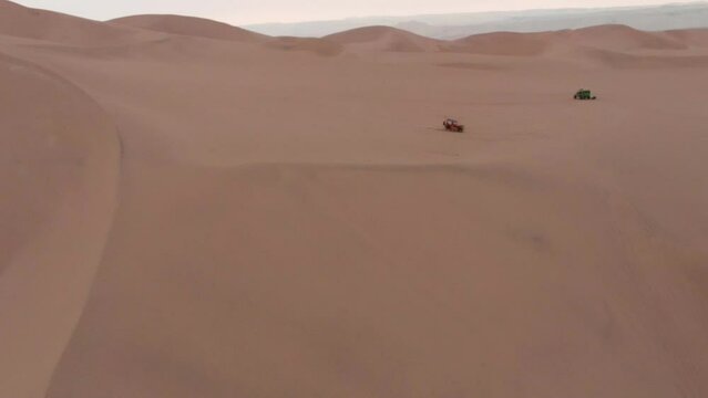 Buggy, jeep driving in huge desert dunes, smooth drone aerial shot. High quality FullHD footage