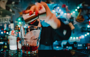 bartender hand making negroni cocktail. Negroni classic cocktail and gin short drink with sweet vermouth, red bitter liqueur and dried orange garnish.