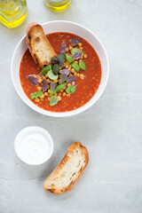 Above view of tomato soup with roasted chickpeas served in a white bowl, vertical shot on a light-grey stone background with space