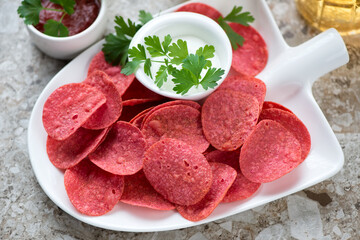 Middle close-up of a shovel-shaped plate with red potato chips and dips, horizontal shot, selective focus