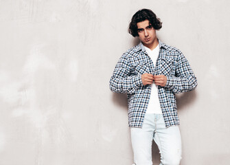 Portrait of handsome confident model. Sexy stylish man dressed in checkered shirt and jeans. Fashion hipster male posing near grey wall in studio. Isolated