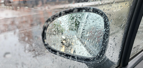 Car side glass view in raining with rain drops on it. Bokeh on rear view mirror car moving amid rain concept