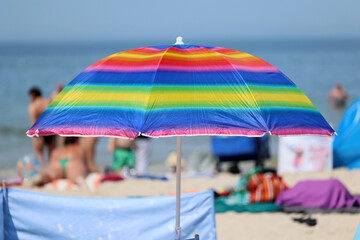 Parasol słoneczny na plaży nadmorskiej w wakacje razem z parawanem na wiatr.
 - obrazy, fototapety, plakaty