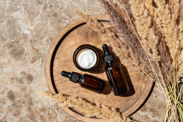 Fototapeta na wymiar Top view of collagen cream in glass jar, serum in amber glass bottle and dry flowers reeds on beige background. Set for skin and body care beauty products.
