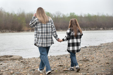 Mom and daughter in identical fashionable plaid shirts for a walk by the river