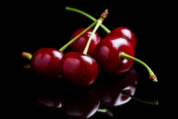 Red cherry berries on a black background with mirror. Three cherries