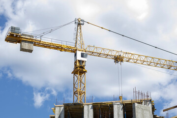 A working construction tower crane against a cloudy sky on a sunny day. The concept of urban development and construction. Industrial background. Crane engineering, construction industry tool.