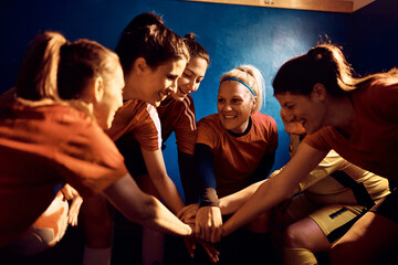 Happy women's soccer team gathering hands in unity in dressing room before the match.