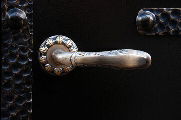 Old stylized bronze door handle on a black steel door