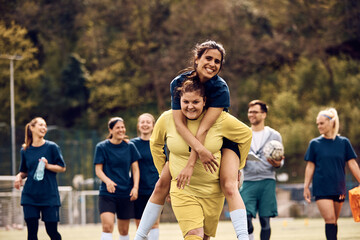 Obraz premium Playful goalkeeper piggybacking her teammate on playing field.