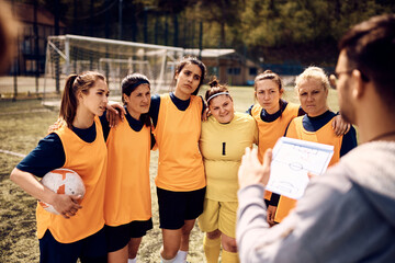 Women's soccer team listening their coach during sports training on playing field.