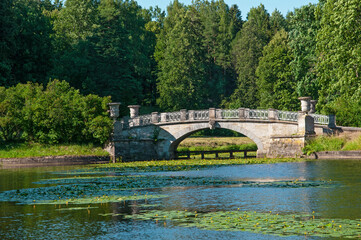 Old gray stone bridge with decorative flowerpots on the river in the summer city public park