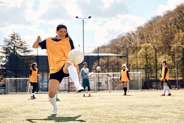 Happy female player practicing with ball during soccer training on playing field.