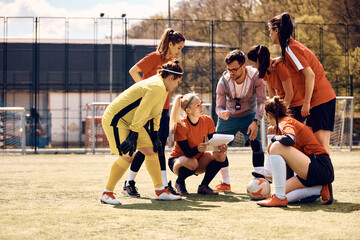 Soccer coach gives instructions to female players on playing field.