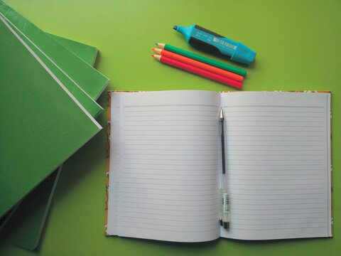 An open book on a green table with big books and stationery