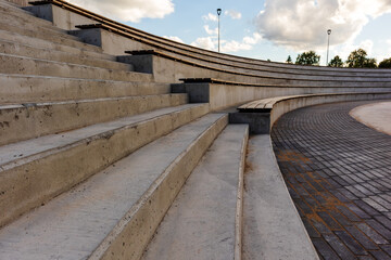 concrete stairs with wooden benches on the stage in the form of a curved arc and a blue sky in the...