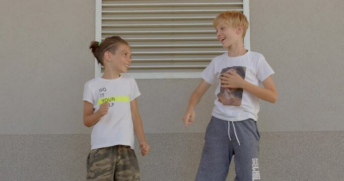 Portrait of happy preteen boys posing together, make dance movements with the body, grey background, summer lifestyle. Schoolchildren rejoice at the beginning of the school year.