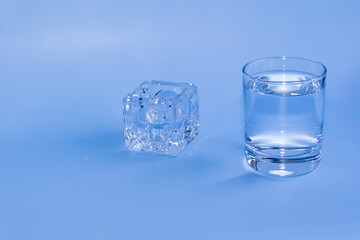 A full glass with clean clear water and an empty container for medicines stands on a blue background.