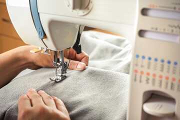 Seamstress female hands holding and stitching gray textile fabric on modern sewing machine at...