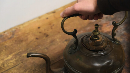 Close-up of man's hand taking an old iron kettle from the wooden board. Concept. Exposition at the...