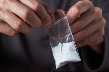 Concept drug addiction. Man hand holds plastic packet or bag with cocaine or another drugs - obrazy, fototapety, plakaty