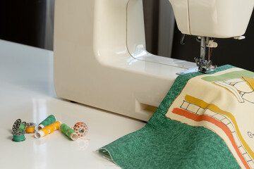 electric sewing machine close-up on a white background sewing green fabric spools of thread bobbin...