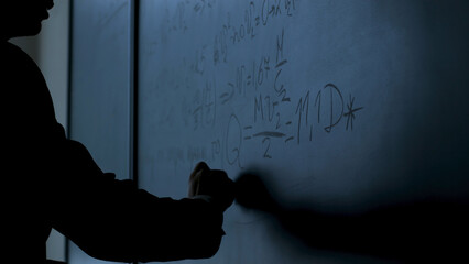 Scientist writing formulas on chalkboard. Hand with chalk wrote physics formulas on black...