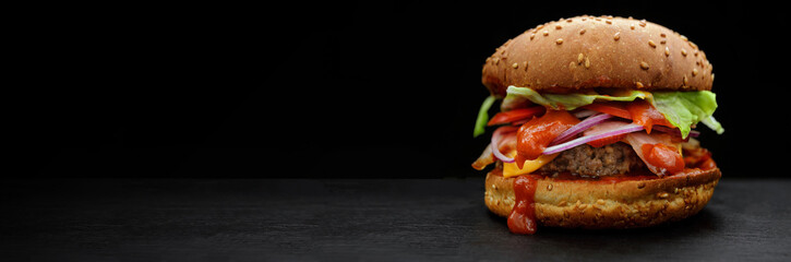 Hamburger with beef, tomato, lettuce, cheese, ketchup and onion on a black background with place for your text. selective focus