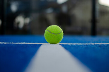 selective focus, a ball on the line of a blue paddle tennis court, racket sports concept