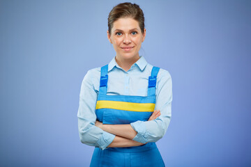 Smiling woman in overalls uniform standing with arms crossed. Isolated female portrait on blue.