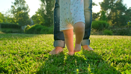 Child learns to take the first steps on the grass. Baby learns to walk with the help of his mother...