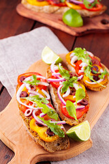 Healthy vegetarian tapas and lime on a cutting board. Vegetarian toasts with tomatoes, greens and olives. Open sandwiches on wooden boards. Top view