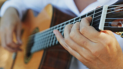Close-up of the musician's playing hands. The guitarist plays the guitar. Professional guitarist plays guitar outdoors. Musician plays a classical guitar in the park. - obrazy, fototapety, plakaty