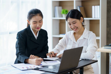 Fototapeta premium Two young Asian businesswomen discuss the concept of a new start-up project. Analyze marketing planning and financial statement at the office.