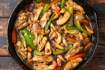Stir fry pepper chicken with sweet peppers, onion, garlic and ginger in iron cast pan
