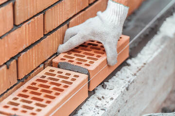 Worker lays brick on cement mortar. Construction of brick fence. Bricklayer at work.