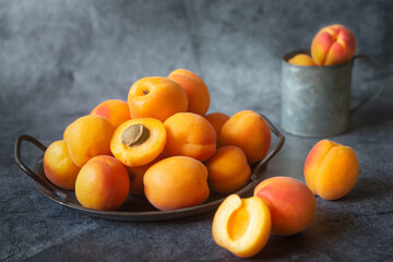 Fresh, ripe apricots in an iron bowl on a gray background.