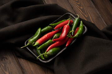 A tray with chili peppers lies on a dark cloth on a wooden table.