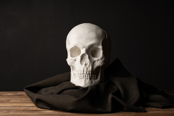A plaster skull wrapped in a dark cloth stands on an oak table.