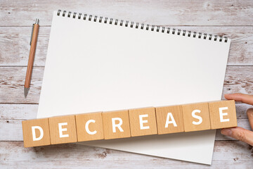 減少・縮小のイメージ｜「DECREASE」と書かれたブロック、ノート、ペン、手
