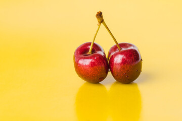 Two juicy berries of a red cherry on a yellow background. Couple of red juicy cherries with stems