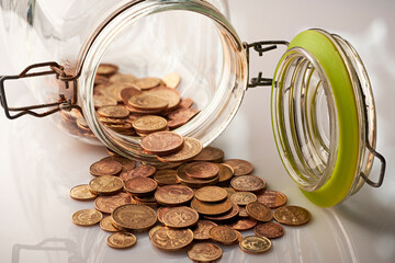 yellow metal coins spilled out of an old glass jar on a white table, macro