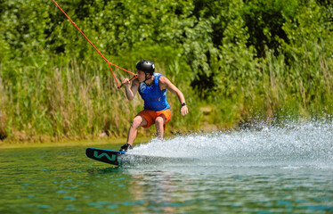 A professional wakeboarder rides on the lake in sunny weather, performing figures