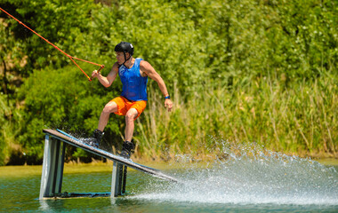 Fototapeta na wymiar A professional wakeboarder rides on the lake in sunny weather, performing figures