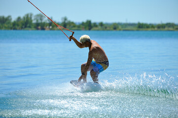 A professional wakeboarder rides on the lake in sunny weather, performing figures