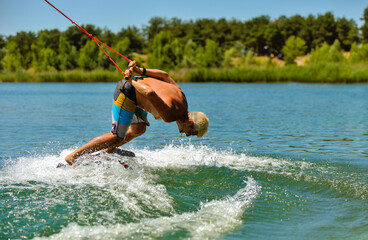 A professional wakeboarder rides on the lake in sunny weather, performing figures