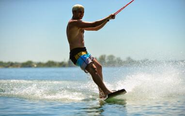 A professional wakeboarder rides on the lake in sunny weather, performing figures