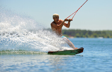 Fototapeta premium A professional wakeboarder rides on the lake in sunny weather, performing figures